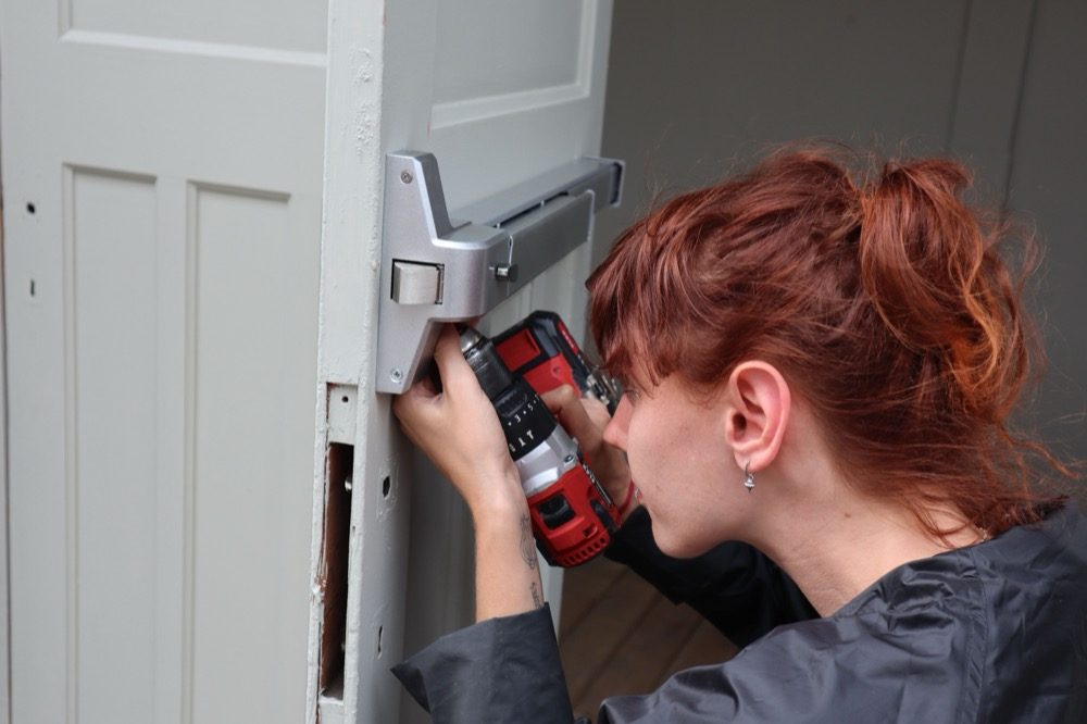 A woman fitting a door with a power drill